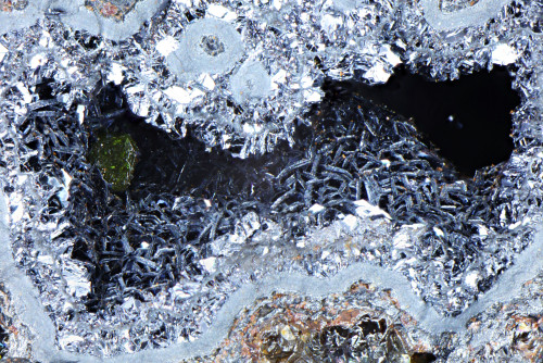 Sharp olive green crystal of bromian chlorargyrite (embolite) on hexagonal crystals of chalcophanite. Width of view 3.5mm. Stack of 70 images.